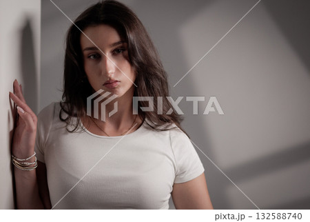 Sad young woman leaning against wall with dramatic shadows 132588740