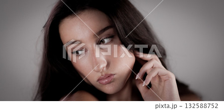 Young woman with long brown hair touching her face and looking away Young woman with long brown hair touching her face and looking away 132588752