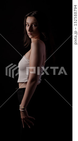 Young woman posing in studio with black background, wearing white top and black pants 132588794