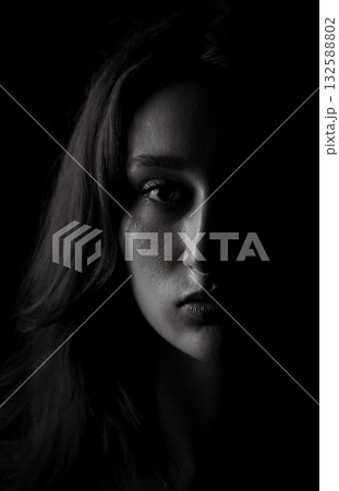 Young woman showing half face emerging from darkness Young woman showing half face emerging from darkness 132588802