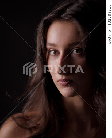 Portrait of young woman with long brown hair showing a serious expression against black background 132588811