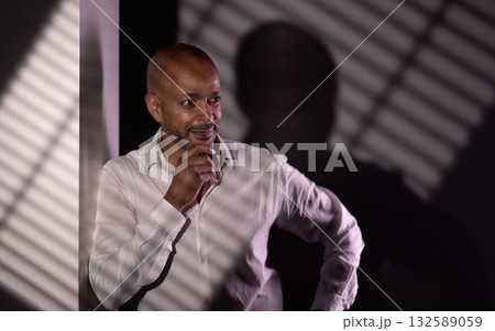 Pensive businessman posing with hand on chin in dark room with striped shadows Pensive businessman posing with hand on chin in dark room with striped shadows 132589059