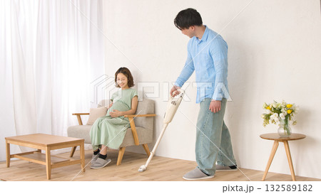 妊婦の女性と話しながら楽しそうに掃除機をかける若い男性 132589182