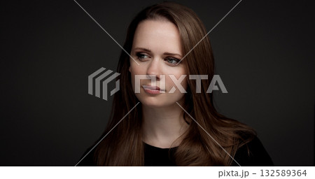 Young woman with long brown hair looking away on a dark background 132589364