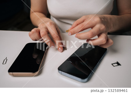 Top view of woman inserting sim card into new smartphone, with another phone and sim ejector tool nearby on white table, during mobile device setup process. Concept of modern technology Top view of woman inserting sim card into new smartphone, with another phone and sim ejector tool nearby on white table, during mobile device setup process. Concept of modern technology 132589461