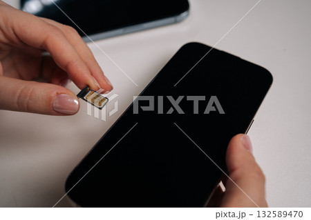 Female hands holding sim card and new smartphone on white table, preparing for inserting sim card and activating mobile service for seamless connectivity, communication. Concept of modern technology Female hands holding sim card and new smartphone on white table, preparing for inserting sim card and activating mobile service for seamless connectivity, communication. Concept of modern technology 132589470