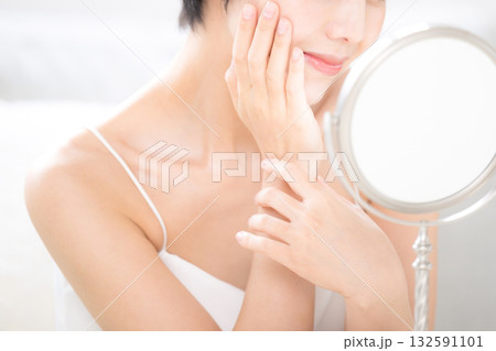 鏡を見る肌のスキンケアを確認する美人な黒髪のショートカットの女性　美容やビューティー、美肌のイメージ 132591101