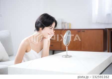 部屋で鏡を見る肌のスキンケアを確認する美人な黒髪のショートカットの女性　美容やビューティー、美肌のイ 132591162