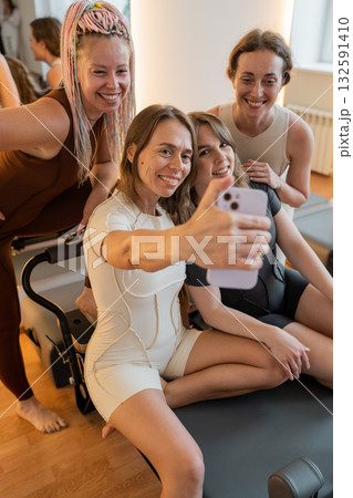 Happy excited pilates girls in sport suits making selfie with trainer after workout in pilates studio 132591410