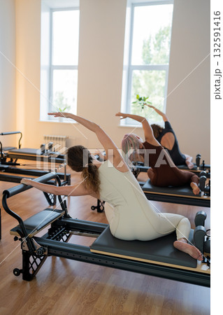 Pilates group of Women doing mermaid exercise in a sunlite modern studio, embodying calm, focus, and strength. 132591416
