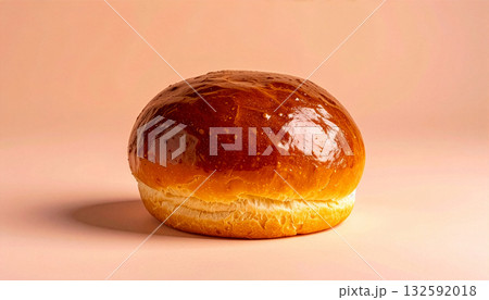 A single, golden-brown brioche bun on a minimal peach-colored background with copy space. 132592018