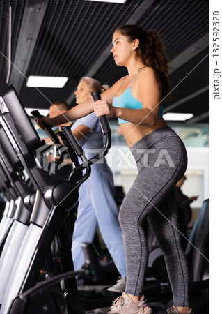 Girl warming up on elliptical machine before training in gym Girl warming up on elliptical machine before training in gym 132592320