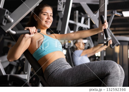 Sporty young girl exercising on chest press machine in gym 132592398