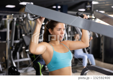 Young woman trains her arm muscles using a simulator in gym Young woman trains her arm muscles using a simulator in gym 132592400