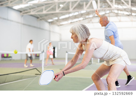 Positive elderly woman playing pickleball on indoor court Positive elderly woman playing pickleball on indoor court 132592669