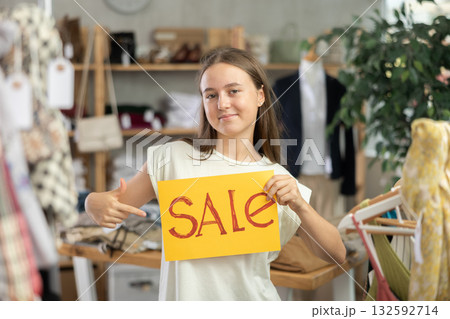 Young teenage girl holding a sign saying Sale in the interior of fashion store 132592714