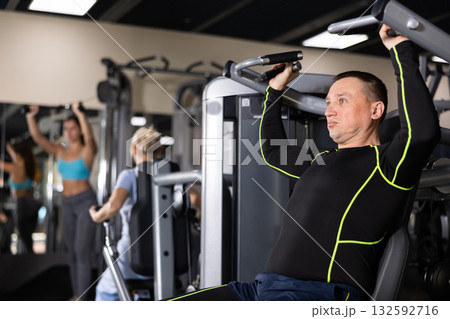 Athlete is engaged in simulator - develops biceps and triceps Athlete is engaged in simulator - develops biceps and triceps 132592716