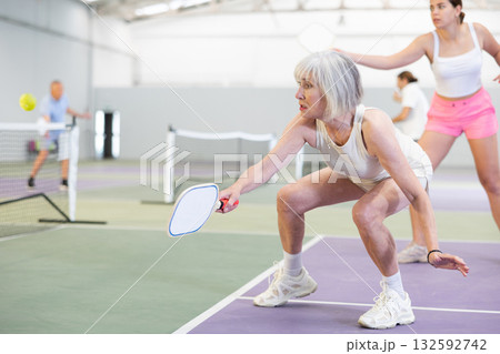 Aged woman playing friendly pickleball match on indoor court Aged woman playing friendly pickleball match on indoor court 132592742
