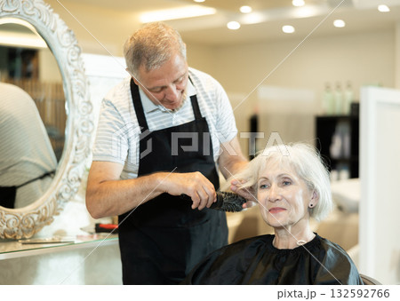 Professional male hairdresser cuts hair of elderly woman at beauty salon Professional male hairdresser cuts hair of elderly woman at beauty salon 132592766