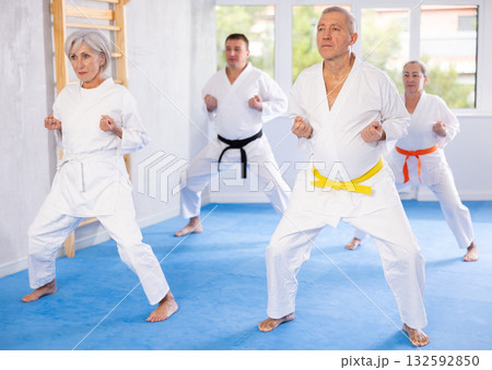 Old man attendee of karate classes practicing kata standing in row with others 132592850