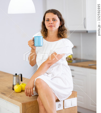 Young attractive girl posing in a white dress with a cup of coffee in modern kitchen 132592895