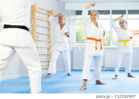 Old woman attendee of karate classes practicing kata standing in row with others Old woman attendee of karate classes practicing kata standing in row with others 132592907