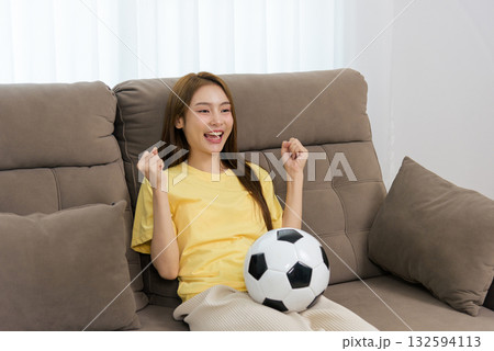 Young happy woman, joyful person, watches activity at home, cheering excitedly with clenched fists, enjoying soccer match on comfortable living room sofa 132594113