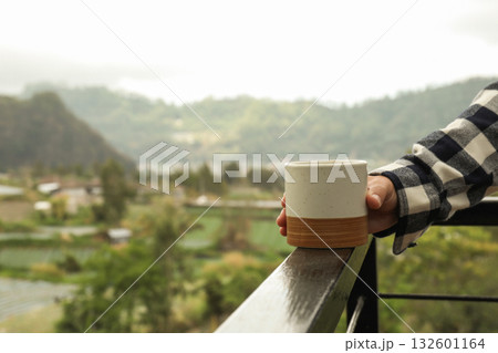 Holding a ceramic cup while admiring the scenic landscape Holding a ceramic cup while admiring the scenic landscape 132601164