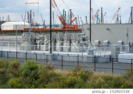 大阪・関西万博会場周辺の夢洲に設置されたGISガス絶縁開閉装置変電所と遠景のクレーン 132601536