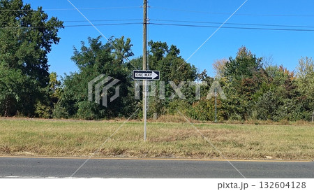 There is a one-way road sign along the highway, and behind it is another road going in the opposite direction, with green trees on the horizon and a clear blue sky. There is a one-way road sign along the highway, and behind it is another road going in the opposite direction, with green trees on the horizon and a clear blue sky. 132604128