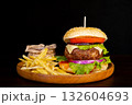 Delicious hamburger with cola and potato fries on a wooden table with a dark brown background behind. Fast food concept. 132604693