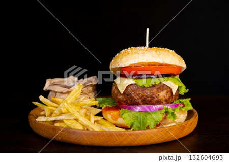 Delicious hamburger with cola and potato fries on a wooden table with a dark brown background behind. Fast food concept. Delicious hamburger with cola and potato fries on a wooden table with a dark brown background behind. Fast food concept. 132604693