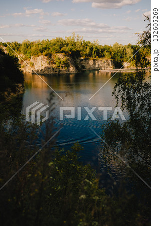 Golden hour sunlight reflecting on Zakrzowek lagoon with trees and cliffs in background, creating serene and peaceful atmosphere in Krakow, Poland. Golden hour on Zakrzowek lagoon, cliffs and trees 132605269