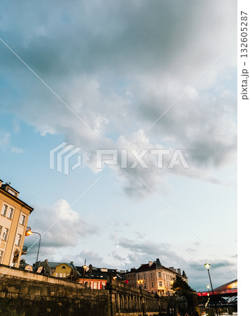 Scenic Krakow cityscape featuring the Vistula River embankment and historic buildings illuminated by stunning sunset under dramatic sky. Krakow cityscape highlighting Vistula River embankment Scenic Krakow cityscape featuring the Vistula River embankment and historic buildings illuminated by stunning sunset under dramatic sky. Krakow cityscape highlighting Vistula River embankment 132605287