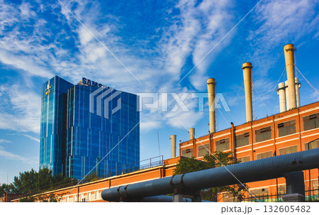 The image shows a modern glass building with a visible logo on its facade, set against a clear blue sky with some clouds. The building appears to be part of an urban landscape. In the foreground 132605482