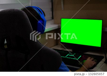 Back view of gamer in computer chair wearing bright headphones in front of a chroma key monitor. Mockup for gaming industry project 132605857