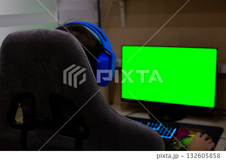 Background for a project about the computer industry. A gamer wearing headphones sits in a gaming chair in front of a monitor. Video games and working on a computer from home 132605858