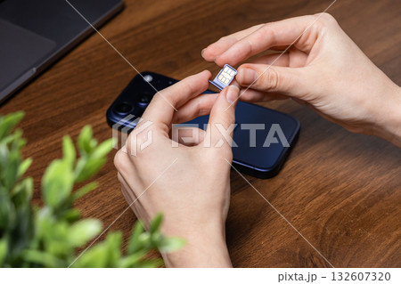 Hands holding a SIM card and tray, preparing for insertion into a smartphone, symbolizing mobile connectivity and digital telecommunication Hands holding a SIM card and tray, preparing for insertion into a smartphone, symbolizing mobile connectivity and digital telecommunication 132607320