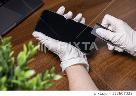Gloved hands carefully applying a protective screen film to a modern smartphone, symbolizing device care and technology maintenance for everyday use Gloved hands carefully applying a protective screen film to a modern smartphone, symbolizing device care and technology maintenance for everyday use 132607322