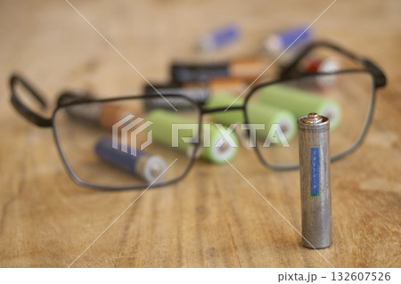 used battery with recycle symbol and eyeglasses on wooden table used battery with recycle symbol and eyeglasses on wooden table 132607526