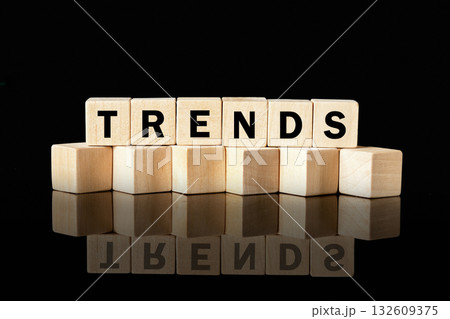 Seven wooden letter blocks stacked on a shiny, reflective surface spell out the word TRENDS against a plain black background. The reflection mirrors the word below 132609375