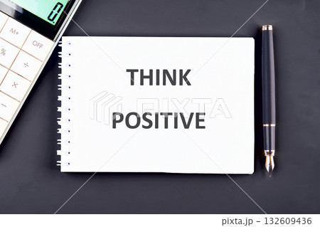 A notepad showing THINK POSITIVE sits on a desk beside a calculator and pen. It encourages a good mindset for upcoming challenges in the Workplace 132609436