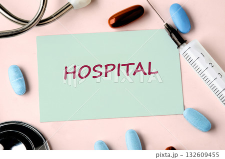Close up shows a note card reading Hospital laying on a table surrounded by pills, a stethoscope, and a syringe, suggesting a medical setting Close up shows a note card reading Hospital laying on a table surrounded by pills, a stethoscope, and a syringe, suggesting a medical setting 132609455