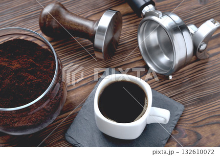 coffee in a cup on a stone stand, a glass jar with coffee and coffee accessories tempera and a coffee machine horn, wooden natural background 132610072