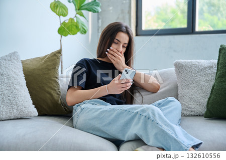 Upset sad young woman looking at smartphone sitting on couch at home 132610556