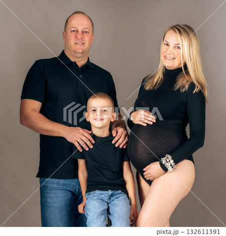Studio family portrait of expecting parents with their son, dressed in black, symbolizing unity and elegance Studio family portrait of expecting parents with their son, dressed in black, symbolizing unity and elegance 132611391