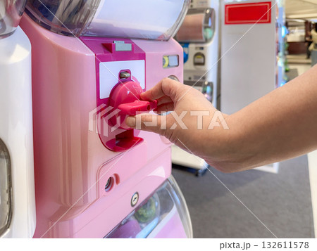A Person Turns the Handle of a Capsule Toy Vending Machine. Capturing the Joyful Anticipation of a Random Surprise on a Bright Monday Morning. 132611578