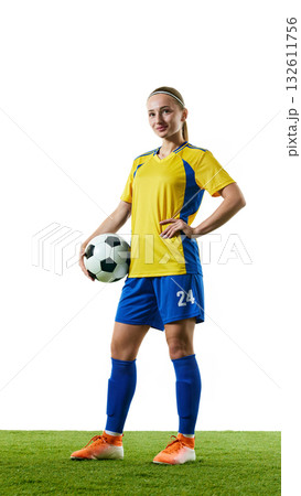 Confident female soccer player in yellow and blue uniform standing on grass field holding ball Confident female soccer player in yellow and blue uniform standing on grass field holding ball 132611756