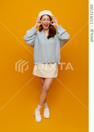 OK gesture cheerful Asian woman making approval sign on yellow background playful happy lifestyle portrait with copy space for advertising branding and social media 132612160