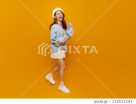Happy Asian woman walking on yellow background wearing blue sweater and beret lifestyle fashion portrait with copy space for social media advertising youth branding and positive campaigns 132612161